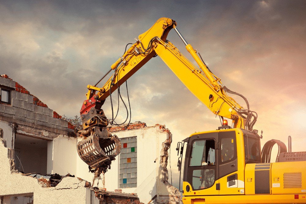 A yellow excavator is being used to demolish a house.